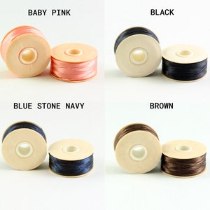 May include: Four spools of thread in different colors: baby pink, black, blue stone navy, and brown. Each spool is wound with thread and has a wooden base.