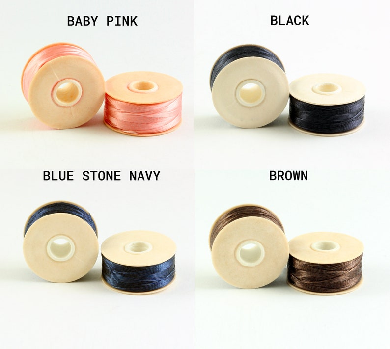 May include: Four spools of thread in different colors: baby pink, black, blue stone navy, and brown. Each spool is wound with thread and has a wooden base.