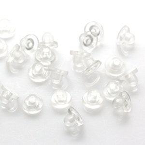 Puede incluir: Primer plano de un montón de respaldos de pendientes de plástico transparente. Los respaldos son pequeños y redondos, con un pequeño poste en el centro. Están diseñados para sujetar los pendientes en su lugar.