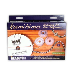 以下が含まれることがあります： ザ・ビーズスミス製の初心者向けクミヒモ編みキット。キットには、クミヒモディスク、糸巻き、留め具、説明書が含まれています。箱は紫で、木製の背景に編まれたコードが描かれています。