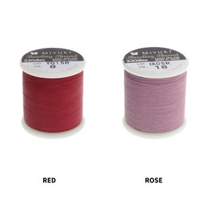 Op de afbeelding: Twee spoelen Miyuki Beading Thread, &eacute;&eacute;n rood en &eacute;&eacute;n roze. De spoelen zijn gelabeld met de merknaam, het type draad, de maat en de kleur. De rode spoel is gelabeld "YG15R 8" en de roze spoel is gelabeld "IXO5R 18".
