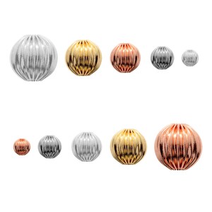 May include: A set of eight round, decorative beads in three different finishes: silver, gold, and rose gold. The beads have a ribbed texture and are arranged in two rows.