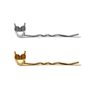 May include: Two hair pins with a heart-shaped setting for a stone. The top pin is silver and the bottom pin is gold.