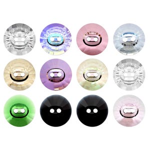 May include: A collection of twelve round, faceted buttons arranged in a grid. Each button features two central holes and a smooth, reflective surface. The colors include clear, iridescent purple, soft pink, light blue, gold, violet, cream, black, and green.