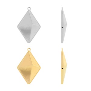 Puede incluir: Dos colgantes en forma de diamante, uno plateado y otro dorado, con una superficie texturizada. Ambos colgantes tienen un bucle en la parte superior para sujetarlos a una cadena.