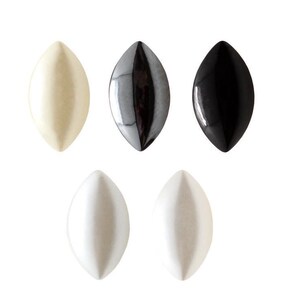 Peut inclure: Cinq cabochons en forme de marquise disposés sur deux rangées. La rangée supérieure comprend une pièce crème, une pièce gris métallique et une pièce noire brillante. La rangée inférieure contient deux pièces blanc mat, toutes aux extrémités lisses et pointues.