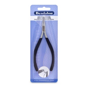 Peut inclure: Une paire de pinces à perles argentées avec des poignées en caoutchouc noir. Les pinces sont emballées dans une plaquette thermoformée en plastique transparent avec une marque bleue et blanche. L'emballage comprend le texte "Beadalon", "Slim Catenos Pliers", "Minco Pierces a Chaine", et "Fines Alices de Punta de Cadena".