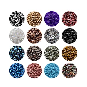 Könnte beinhalten: Sechzehn kreisförmige Anordnungen kleiner, unregelmäßig geformter Perlen in verschiedenen Farben. Zu den Farben gehören Schwarz, Gold, Lila, Rot, Irisierend, Braun, Silber und Schwarz. Weitere Farben sind Blau, Dunkelbraun, Grün und Gold. Die untere Reihe zeigt blaue, rosa und türkisfarbene Perlen.