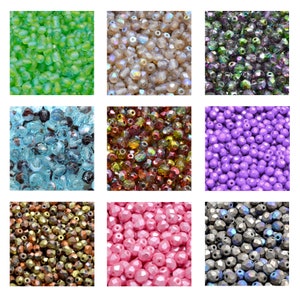 Puede incluir: Surtido de cuentas de vidrio en varios colores y acabados, incluyendo transparente, verde, morado, rosa, marrón e iridiscente. Las cuentas están dispuestas en un patrón de cuadrícula.