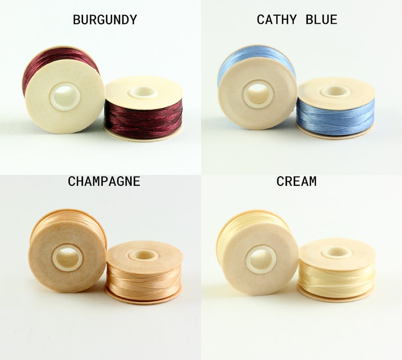 May include: Four spools of thread in different colors: burgundy, blue, champagne, and cream. Each spool is wound with thread and has a wooden base.