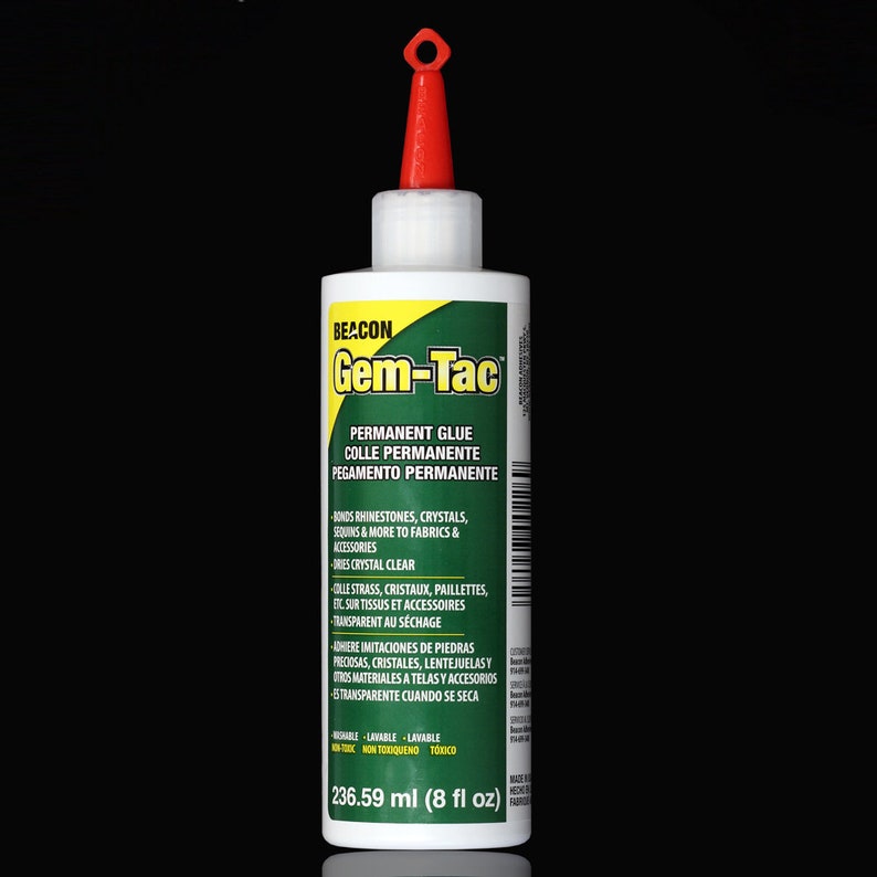 May include: A bottle of Beacon Gem-Tac permanent glue. The bottle is white with a green label that says "Gem-Tac" in yellow letters. The label also says "Permanent Glue" and "Colle Permanente" in black letters. The bottle is 236.59 ml (8 fl oz).