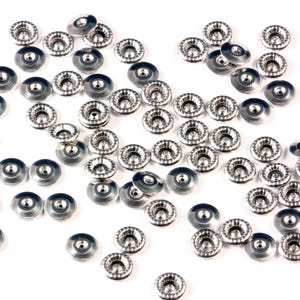 May include: A large group of silver metal decorative embellishments with a raised, textured center. The embellishments are scattered on a white surface.