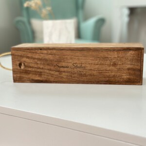 May include: A wooden box with a brown stain and the text "Signature Studios" engraved on the top.