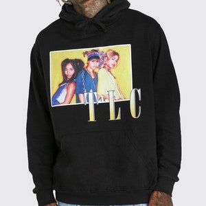 May include: Black hooded sweatshirt with a graphic print of a yellow rectangle with three women in it. The text "TLC" is printed below the rectangle in gold.