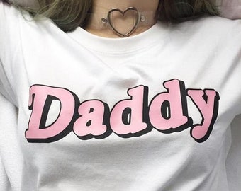 May include: White t-shirt with the word "Daddy" printed in pink letters with black outlines.