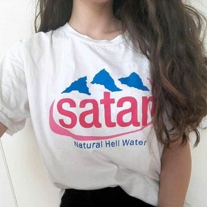 May include: White t-shirt with a pink and blue graphic that says "satan Natural Hell Water".
