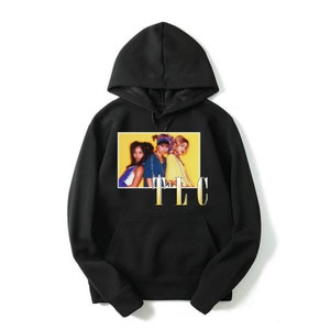 May include: Black hooded sweatshirt with a graphic print of the R&B group TLC. The image is on a yellow background with the group's name in gold letters below the image.
