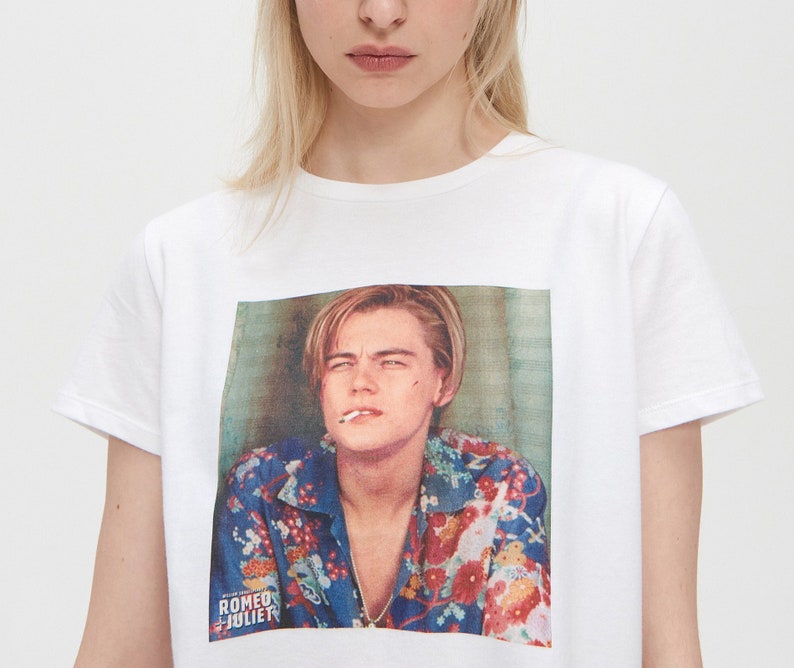 May include: White t-shirt featuring a printed image of Leonardo DiCaprio wearing a floral shirt and smoking a cigarette. The text "ROMEO + JULIET" is printed below the image.