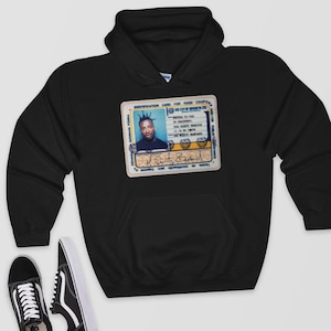May include: Black hooded sweatshirt featuring a graphic of an ID card with a photo of a person and the text "The City of Brooklyn Zoo." The ID card has blue and yellow accents. The sweatshirt has a front pocket and a hood.