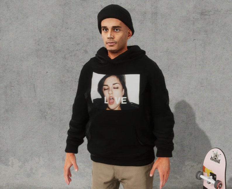May include: A black hoodie with a graphic print of a woman's face and the word "LOVE" on the front. The person wearing the hoodie is also wearing a black beanie.