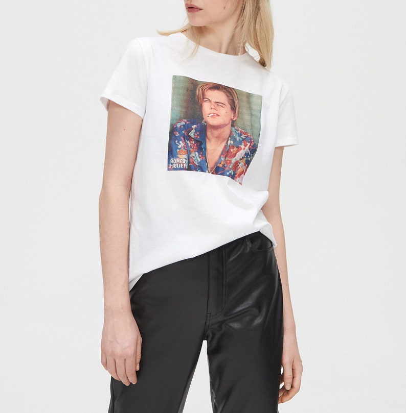 May include: White t-shirt featuring a graphic print of Leonardo DiCaprio wearing a floral shirt. The text "Romeo + Juliet" is printed below the image.