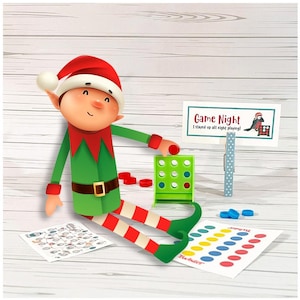 May include: An elf figure wearing a red and green outfit is surrounded by board games. A green Connect Four game, red and blue game pieces, and a Twister mat are visible. A sign reads "Game Night" with the text "I stayed up all night playing!"