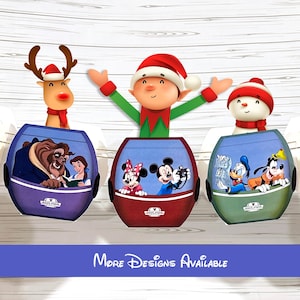 May include: Three Disney Skyliner gondola ornaments featuring characters from Beauty and the Beast, Mickey and Minnie Mouse, and Donald Duck with Goofy. An elf, a reindeer, and a snowman are positioned above the gondolas. Text reads More Designs Available.