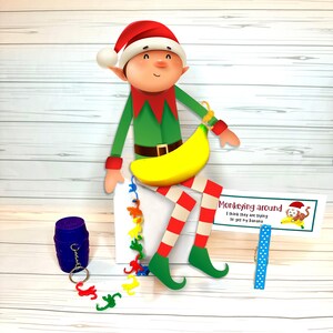 May include: A whimsical elf figure with a red hat, green tunic, and striped red and white legs, holding a yellow banana. A sign reads "Monkeying around I think they are trying to get my banana". Includes a blue barrel and monkey-shaped keychains.