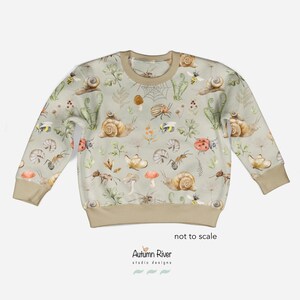 May include: A light green sweatshirt with a pattern of snails, ladybugs, ants, mushrooms, and bees. The text "Autumn River studio designs" is printed on the bottom of the sweatshirt.