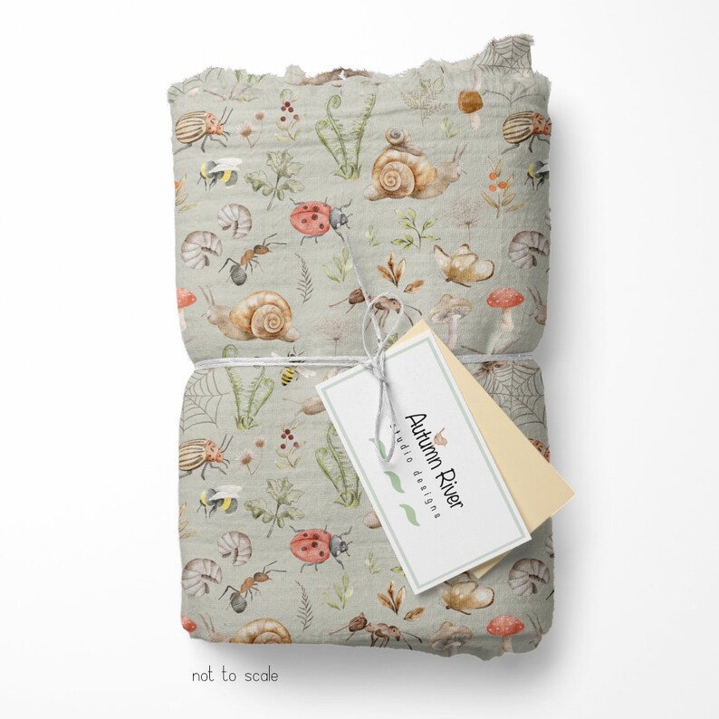 May include: A roll of fabric with a light gray background and a repeating pattern of watercolor illustrations of snails, ladybugs, ants, bees, mushrooms, and ferns. The fabric is tied with a white string and a tag that reads "Autumn River Studio Designs".