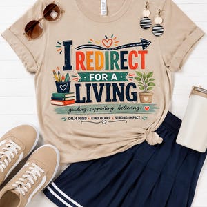 May include: A beige t-shirt with the text "I REDIRECT FOR A LIVING" in colorful letters. The shirt is paired with a navy blue skirt, tan sneakers, and sunglasses. The text also includes the phrases "guiding, supporting, believing" and "CALM MIND KIND HEART STRONG IMPACT."