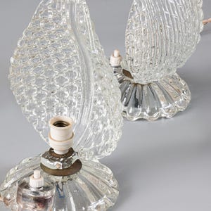 May include: A pair of clear glass table lamps featuring textured leaf-shaped shades and fluted circular bases. Each lamp includes a central light socket, a small white push-button switch, and a light-colored twisted fabric electrical cord.