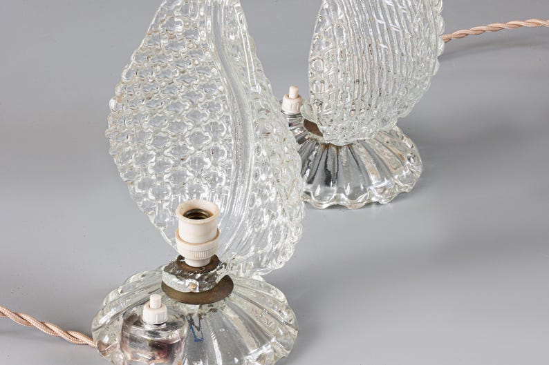 May include: A pair of clear glass table lamps featuring textured leaf-shaped shades and fluted circular bases. Each lamp includes a central light socket, a small white push-button switch, and a light-colored twisted fabric electrical cord.