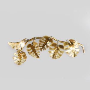 Op de afbeelding: Gouden metalen wanddecoratie met een wijnstok met meerdere bladeren in een tropische blader vorm.
