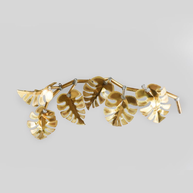 Op de afbeelding: Gouden metalen wanddecoratie met een wijnstok met meerdere bladeren in een tropische blader vorm.
