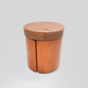 May include: A round wooden stool with a brown leather top. The stool is made of wood and has a simple design.