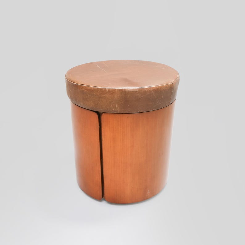 May include: A round wooden stool with a brown leather top. The stool is made of wood and has a simple design.