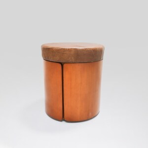 May include: A round wooden stool with a brown leather top. The stool is made of wood and has a simple design.