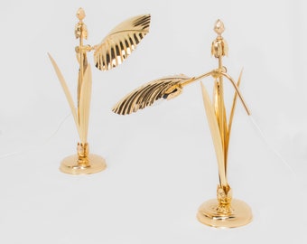 May include: Two gold table lamps with a palm leaf design. The lamps have a gold finish and a white cord.