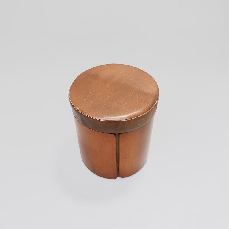 May include: A brown wooden stool with a leather top. The stool is round and has a simple design.