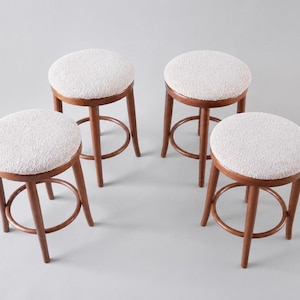 Può includere: Quattro sgabelli da bar in legno con sedute rotonde e strutturate color bianco sporco. Gli sgabelli hanno una finitura marrone scuro e un poggiapiedi circolare. Design moderno e minimalista.