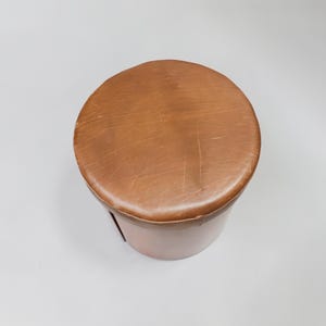 May include: A brown leather ottoman with a round top and a cylindrical base.