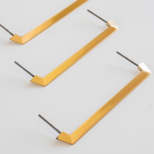 May include: Three gold-toned metal cabinet pulls with a rectangular shape and angled edges. Each pull has a screw on one end.