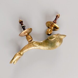 May include: Two antique brass door handles. One handle is shaped like a bird with a long tail and a textured body. The other handle is a matching design. Each handle has a bolt and a round backplate for mounting.