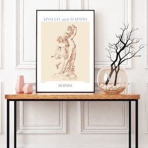 May include: A black framed print of a line drawing of the sculpture "Apollo and Daphne" by Bernini. The print is on a beige background and features the title of the artwork and the artist's name.