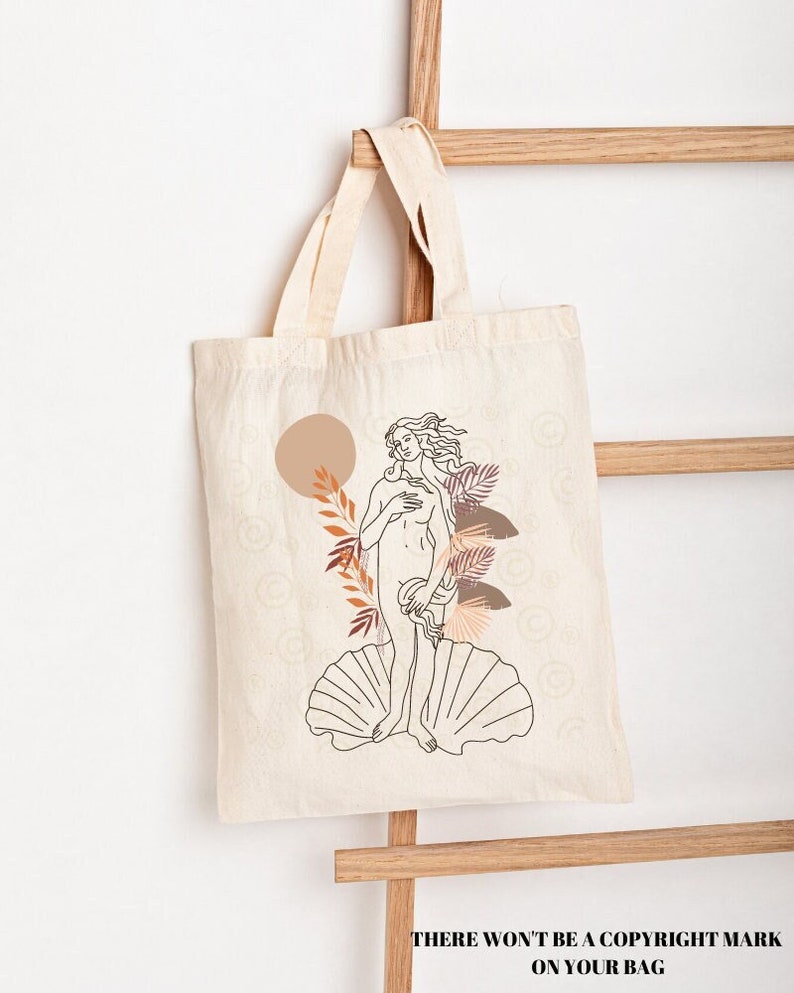 Peut inclure: Un sac fourre-tout en toile blanche avec un dessin au trait d'une femme debout sur une coquille Saint-Jacques. La femme est entour&eacute;e de feuilles stylis&eacute;es et d'un soleil dans des tons orange et brun.