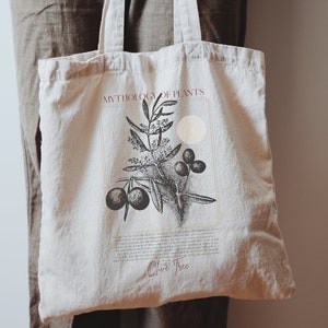 Pode incluir: Uma bolsa de tecido branca com ilustra&ccedil;&otilde;es em preto e branco de uma oliveira e azeitonas. O texto "MYTHOLOGY OF PLANTS" e "Olive Tree" est&aacute; impresso em vermelho na bolsa. O texto "THERE WON'T BE A COPYRIGHT MARK ON YOUR BAG" est&aacute; impresso na parte inferior da bolsa.
