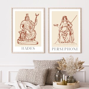 May include: Two framed illustrations of Greek gods, Hades and Persephone, in a red-brown color scheme. The illustrations are set against a cream background and feature detailed line drawings of the figures.