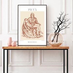 May include: A black framed print of a line drawing of Michelangelo's Pieta sculpture. The drawing is in brown on a cream background. The title "PIETA" and the artist's name "MICHELANGELO" are printed below the drawing.