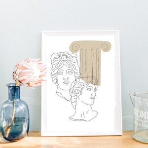 May include: Line art print of two classical busts with a beige column behind them. The print is framed in a white frame and is on a wooden surface.